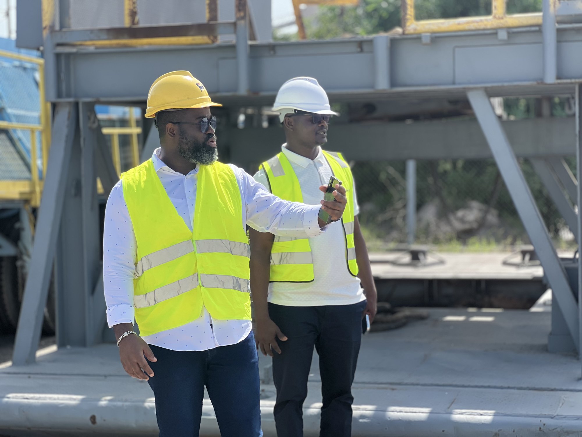 Two members of the inspection party in hard hats and high-visibility vests in front of the drilling rig structure in Ghana